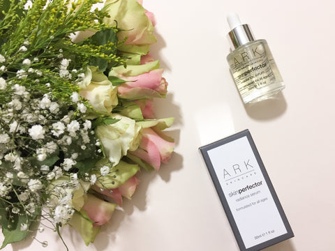 Flatlay of ARK Skincare's Radiance Serum and carton laid beside some flowers