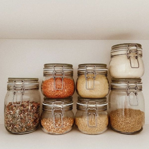 Image: 7 mason jars stacked in a kitchen cupboard filled with ingredients such as lentils, rice and sugar. 