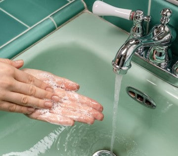 person washing their hands in a teal sink under running water
