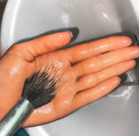 Image: Make-up brush being washed with cleanser in the palm of persons hand