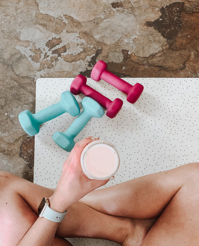 Image of a woman sat cross legged on a exercise mat with dumbbells and smoothie