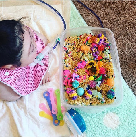 child with holoproencephaly using EazyHold universal cuff with a sensory bin