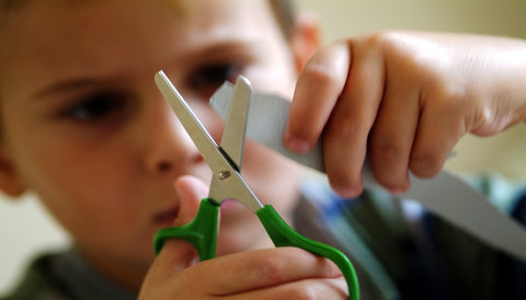 child using bilateral coordination to hold a paper and cut it with scissors