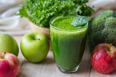 Green smoothie surrounded by apples and leafy greens