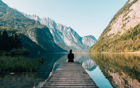 Person sitting at the edge of a dock surrounded by mountains