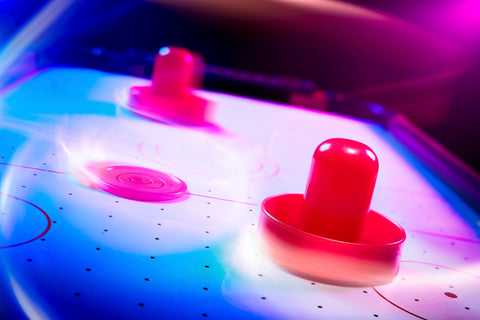 Blurred mallets on a top 10 air hockey table with black lighting.