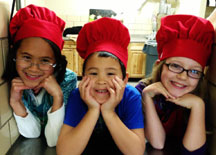 Three young students wearing red chefs hats.