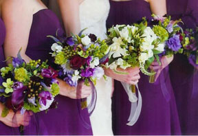 Bbride holds a white bouquet, flanked by bridesmaids holding purple bouquets
