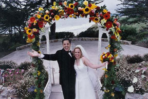Bride and groom gaily standing under a wedding arch densely colored with flowers - Renee's Garden 