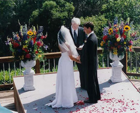 A birde and groom getting married in front of large flower arrangements