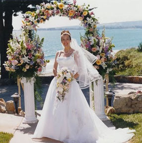 A bride under a dense flower arrangement wedding arch - Renee's Garden