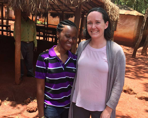 Erin and a Tanzanian woman smiling with an orange dirt background