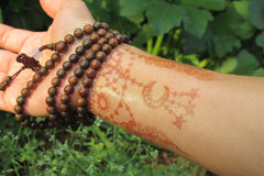 alt = "yoga intention mala beads henna sun gold mica shimmer favorite words brown hand wrist"