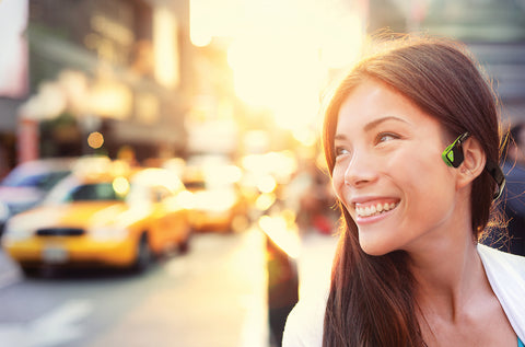 Woman walking in city with ivy green bone conduction headphones