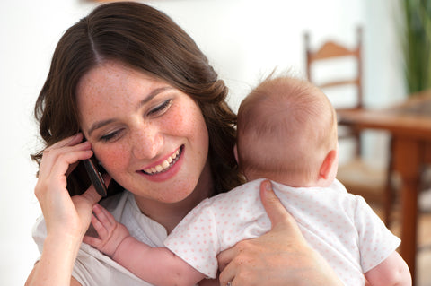 Mother on phone and holding baby | Safe Sleep Space