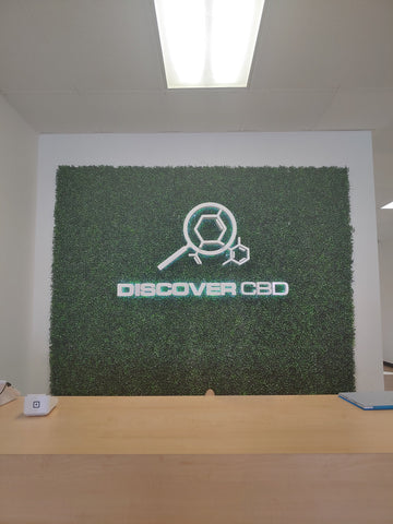 brown store counter with green grass wall sign on white wall with Discover CBD logo