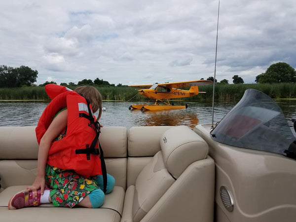 girl wearing life jacket looks at seaplane from boat