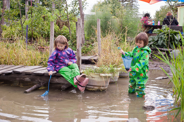 Biddle and Bop kids sitting in pond at Ithaca Children's Garden in Biddle and Bop waterproof gear