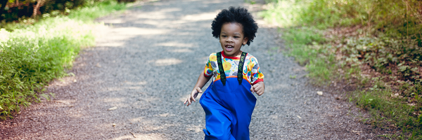 child running down path wearing blue rain bibs