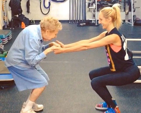 anciana haciendo sentadillas asistida por entrenadora