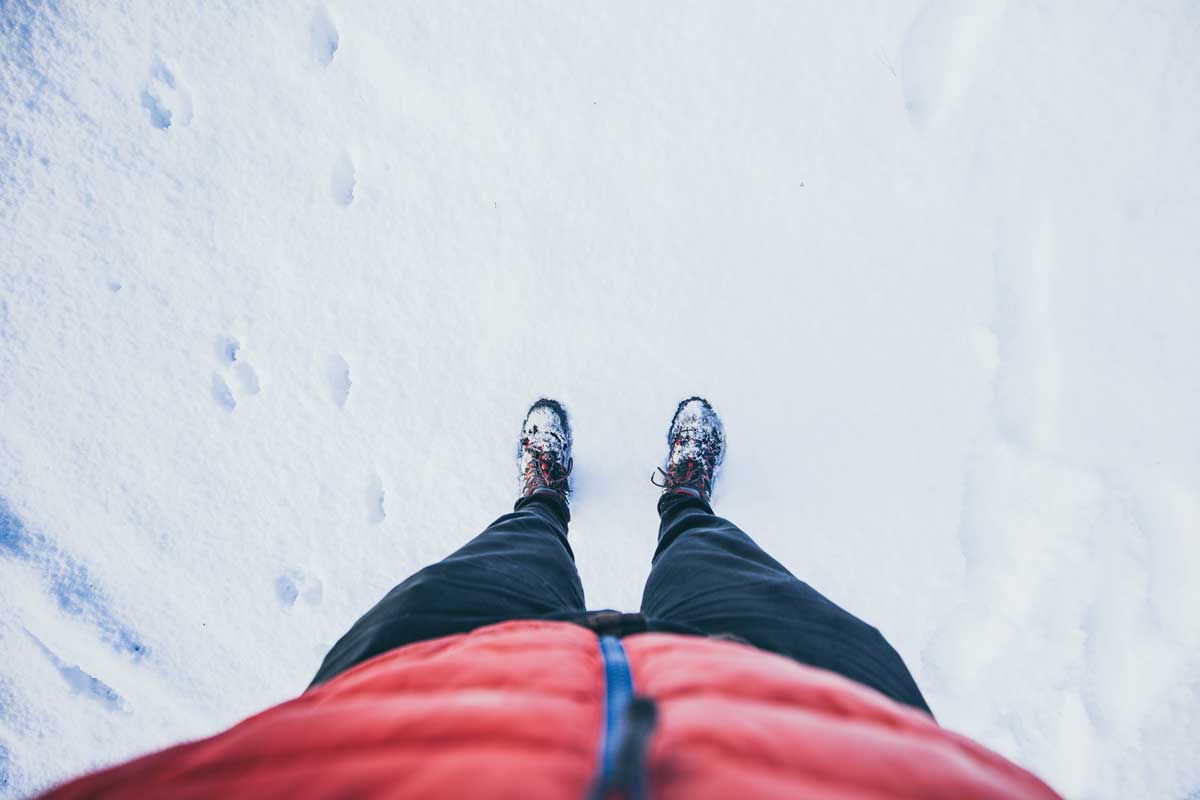 Hiker looking down at feet while standing in the snow.