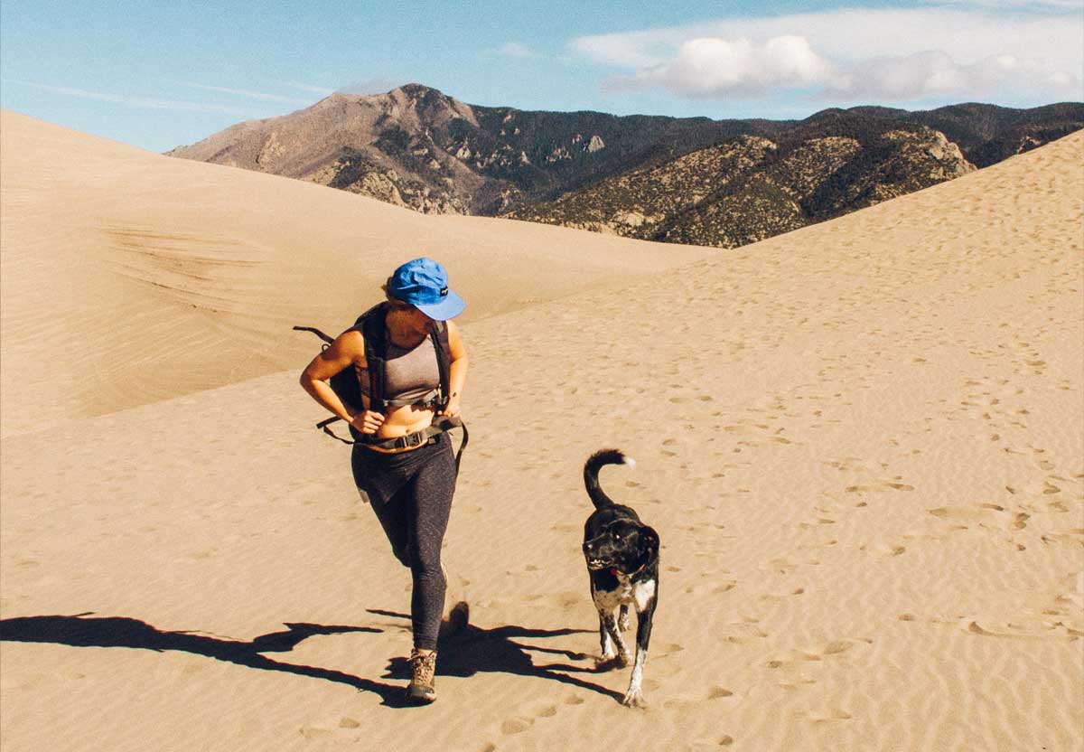 Women and her dog hiking through desert.