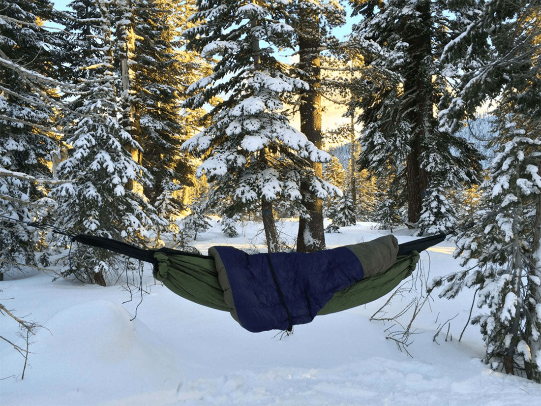 Thick sleeping bag in a hammock while camping in a snowy forest.