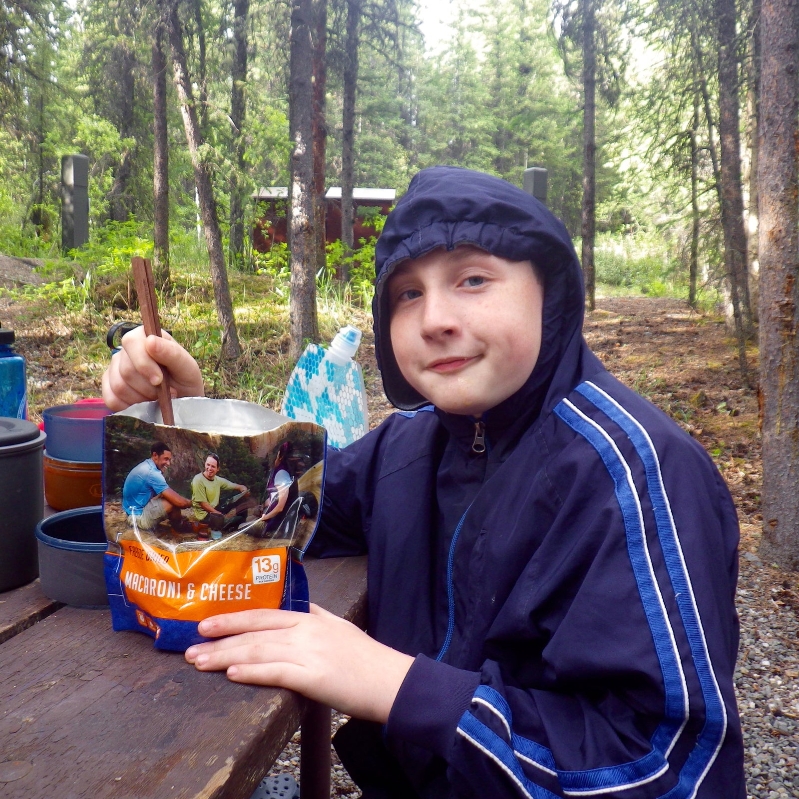 Close up of kid eating a backpacking meal at a camp picnic table.