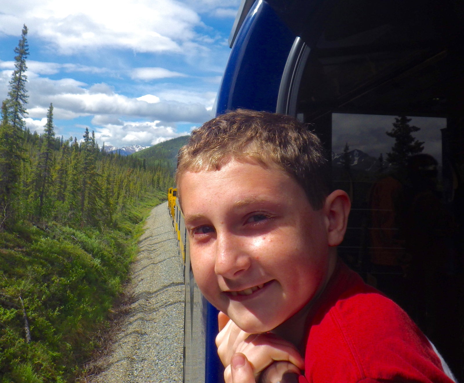 Close up of boy smiling as he leans out of a train in the woods.