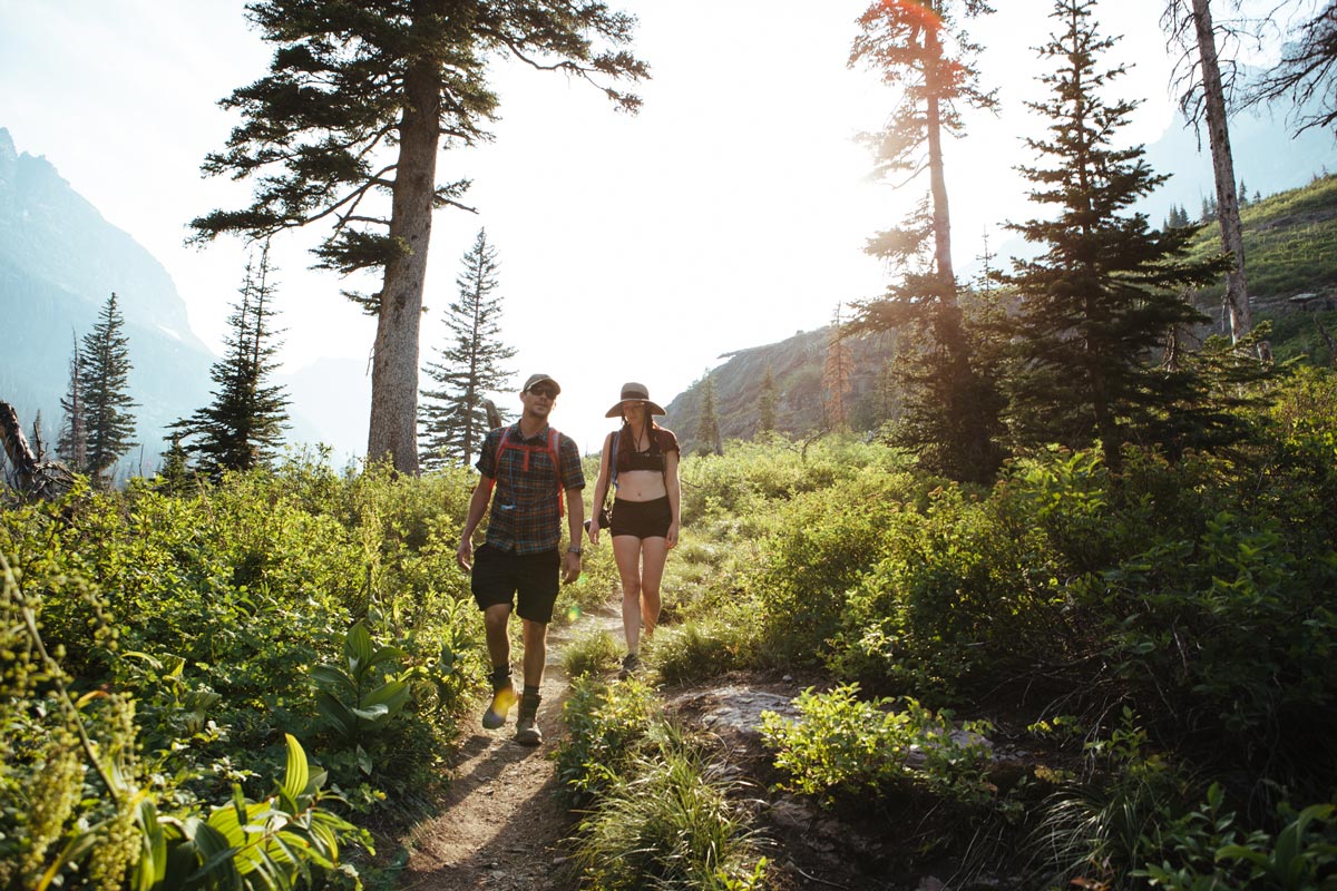 Man and a women chatting as they hike on a wooded mountain side trail.