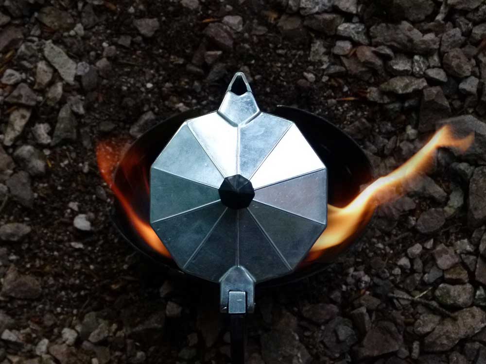 Coffee percolator brewing over a camp stove viewed from above.