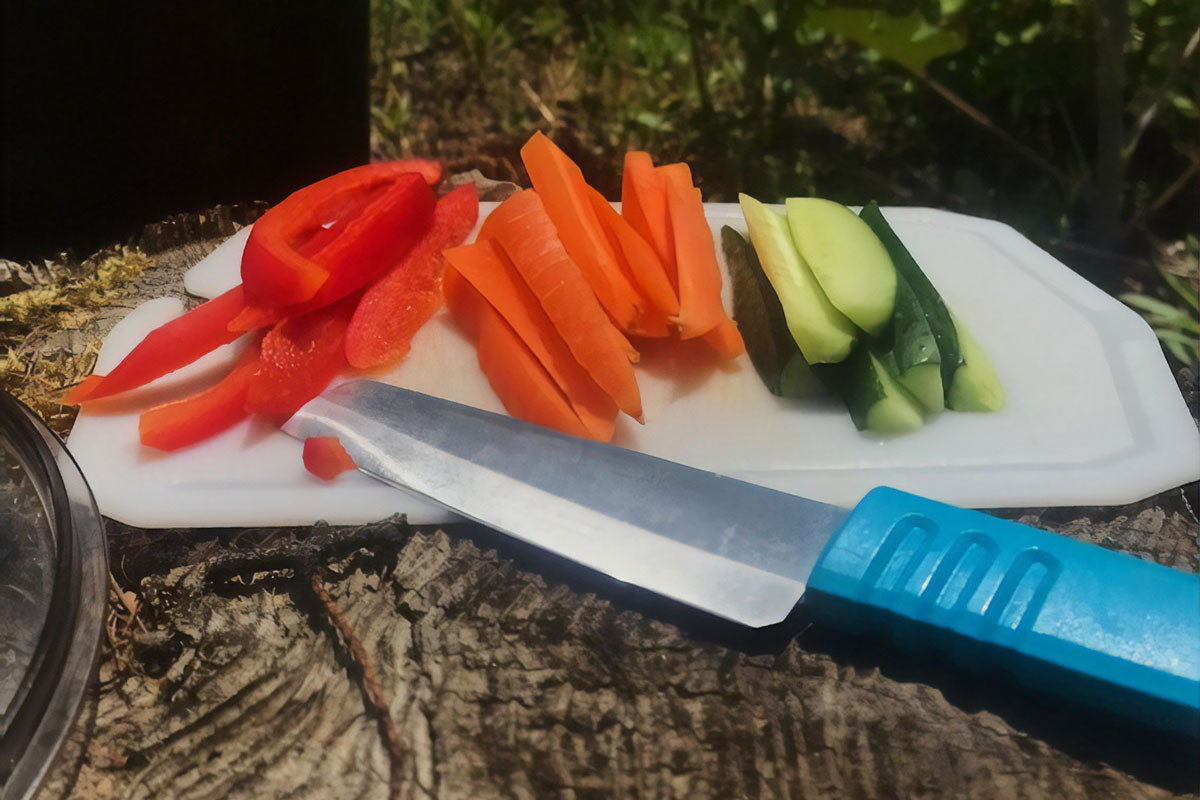 Cutting board sitting on log with knife and freshly cut veggies.