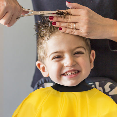 smiling boy having haircut whilst wearing a neocape yellow childs gown