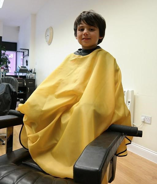 child sitting in salon chair wearing yellow childs neocape gown