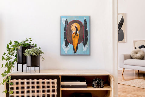 Painting of a stylized woman with dark hair and feathers on a blue background hanging on a white wall above a wooden cabinet