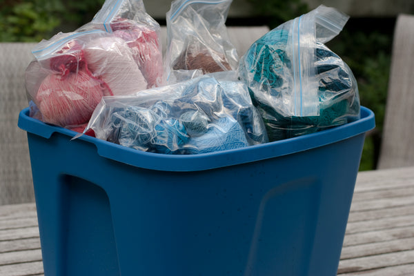 Blue rubbermaid tub overflowing with ziploc bags full of yarn scraps, sorted by colour