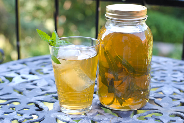 Glass of green iced mint tea beside mason jar