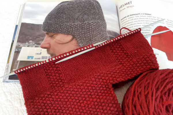 Knitted viking helmet style hat in red yarn in progress on knitting needles