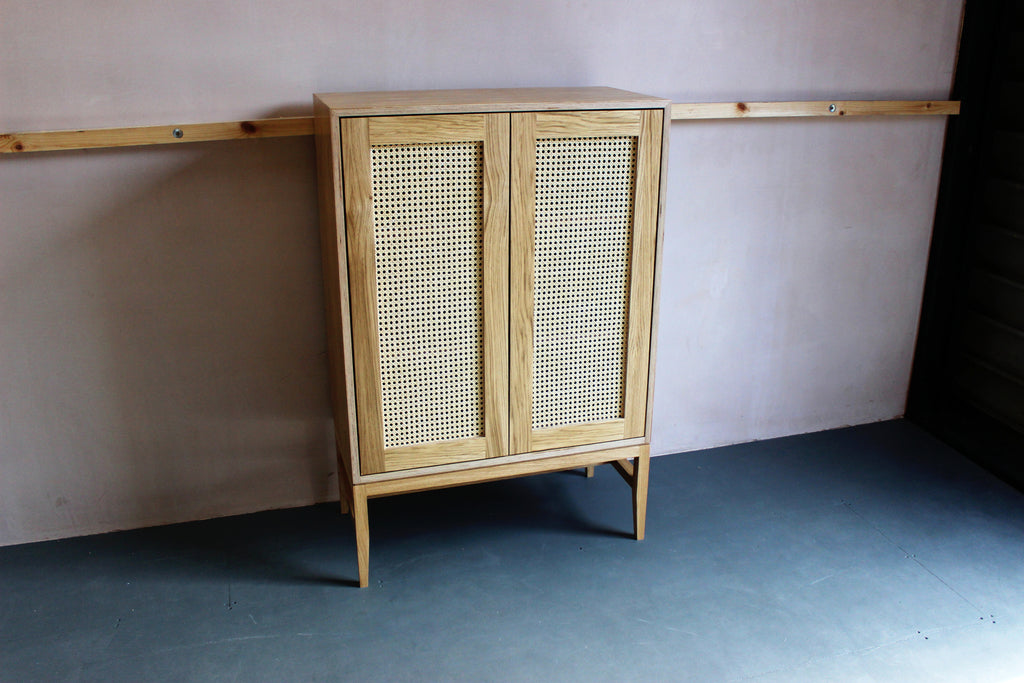 Mid-century style rattan cane cabinet featuring oak veneered plywood, solid oak legs and woven cane in-lay. Designed and made by Jon Grant London in Leyton, East London.