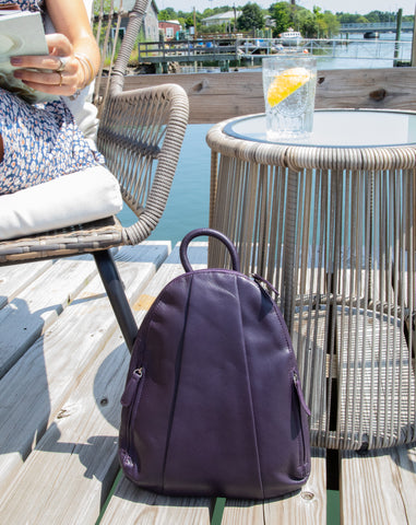 teardrop multi zip backpack in plum leaning against outdoor table