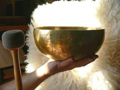Striking a singing bowl with a professional felt mallet rather than rubbing it.