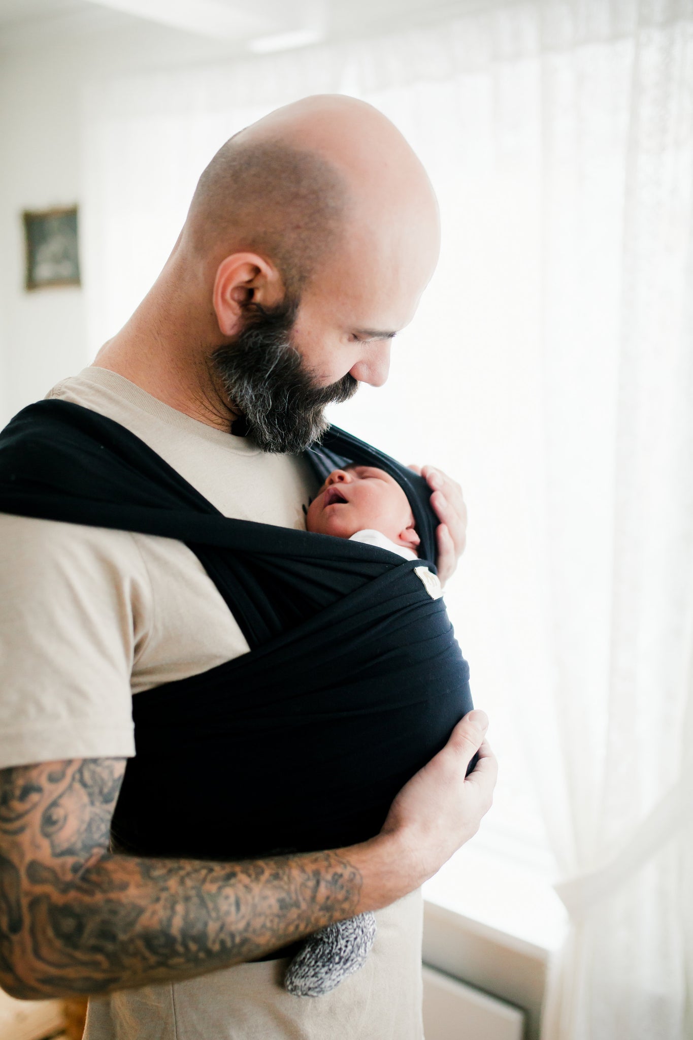 Father, baby wearing daddy holding newborn baby in black newborn baby wrap. 