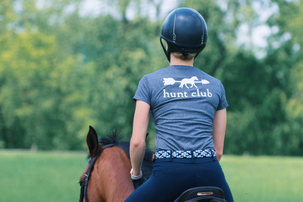 An equestrian riding a horse wearing a grey shirt. 