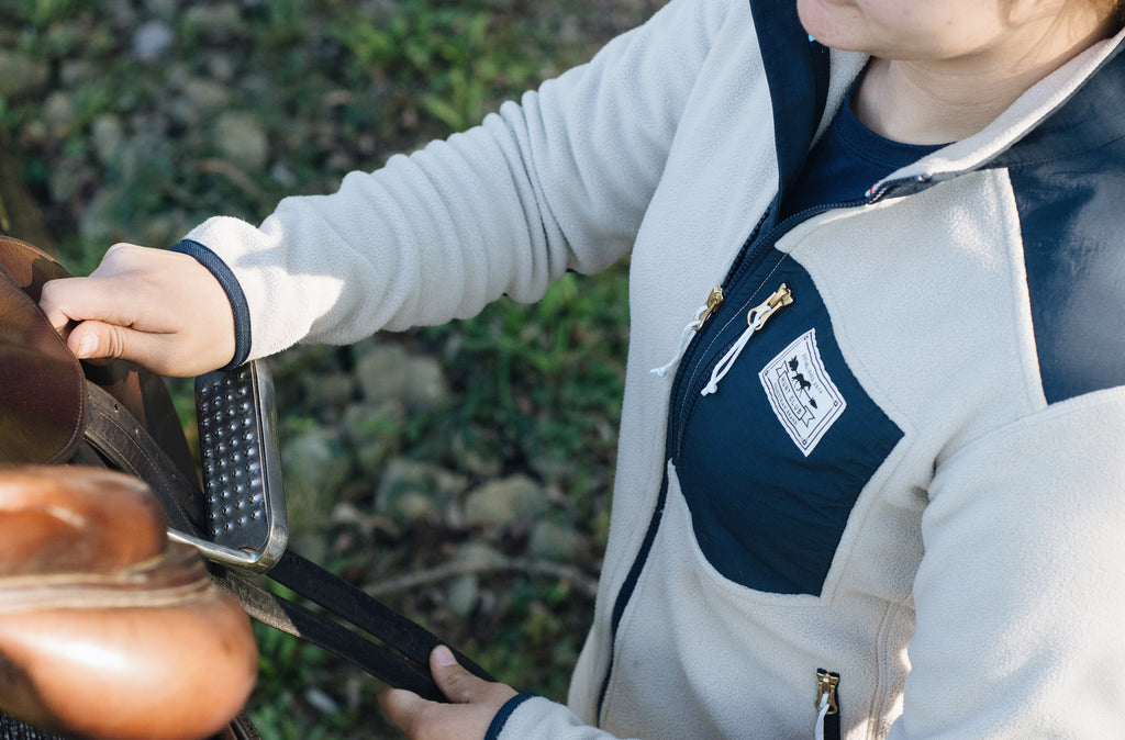 An equestrian adjusting her saddle in the Hunt Club oatmeal fleece jacket