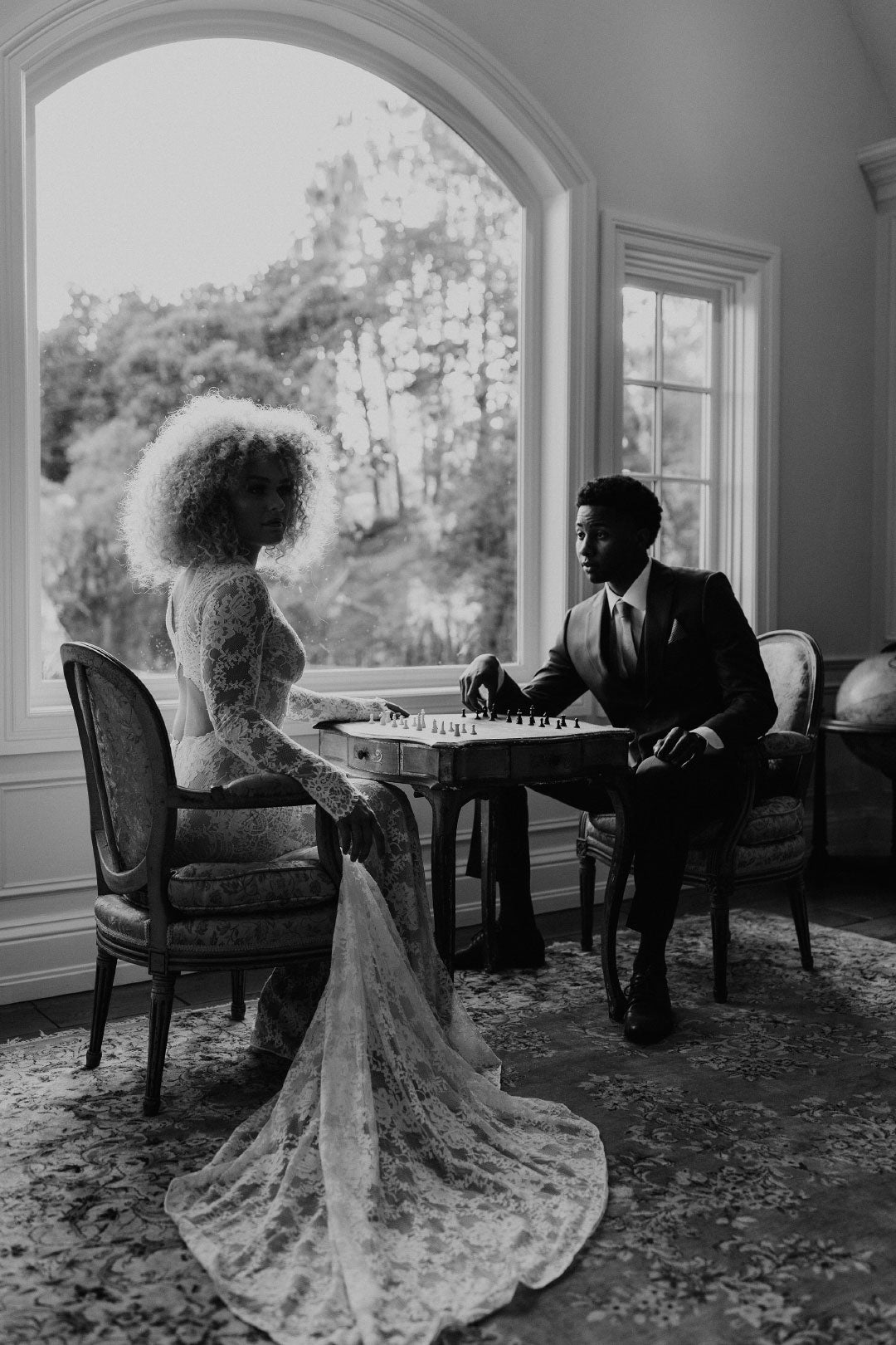 Bride and Groom seated by large window playing chess