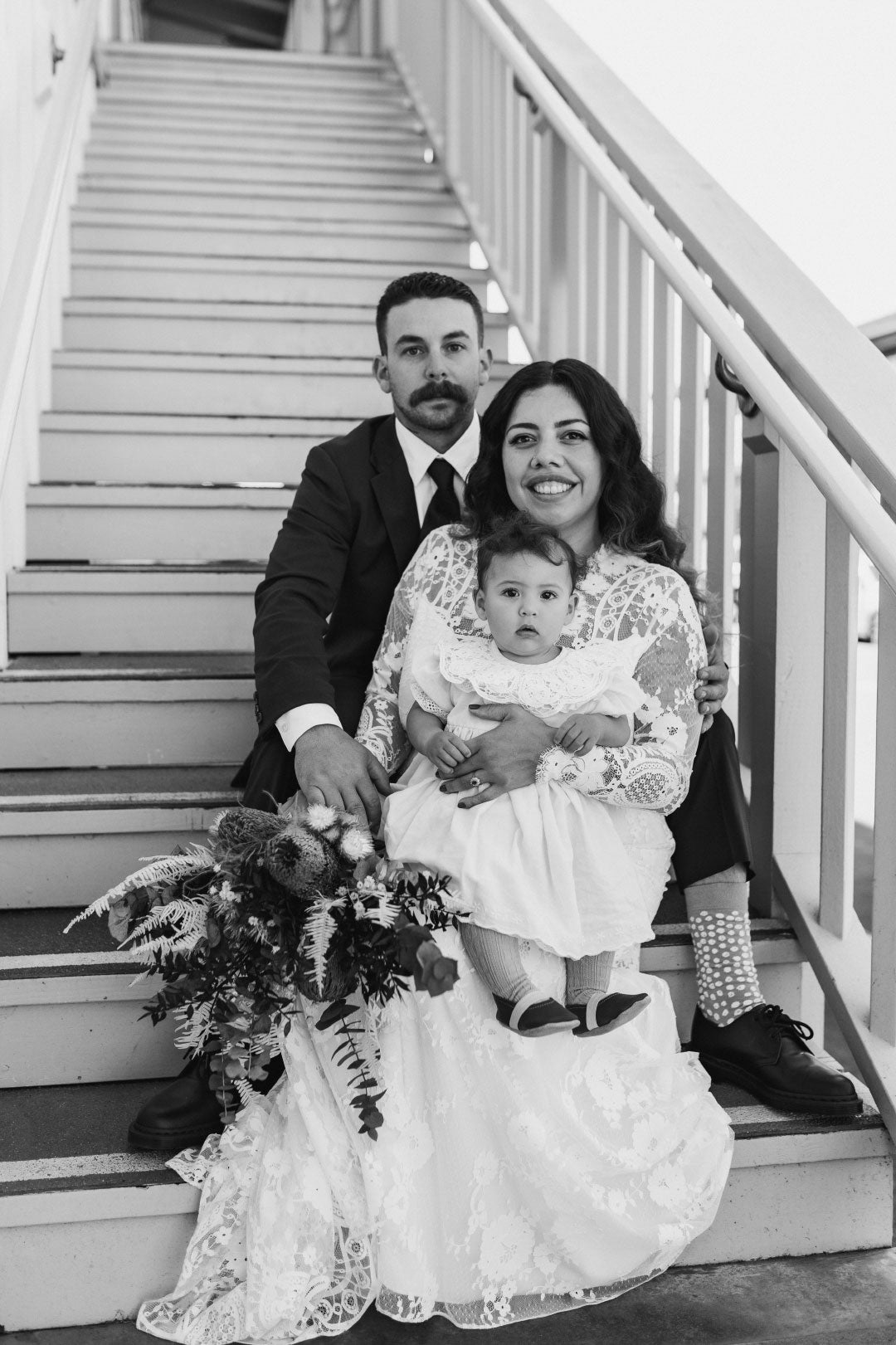 Groom and Bride sitting on stairs with baby
