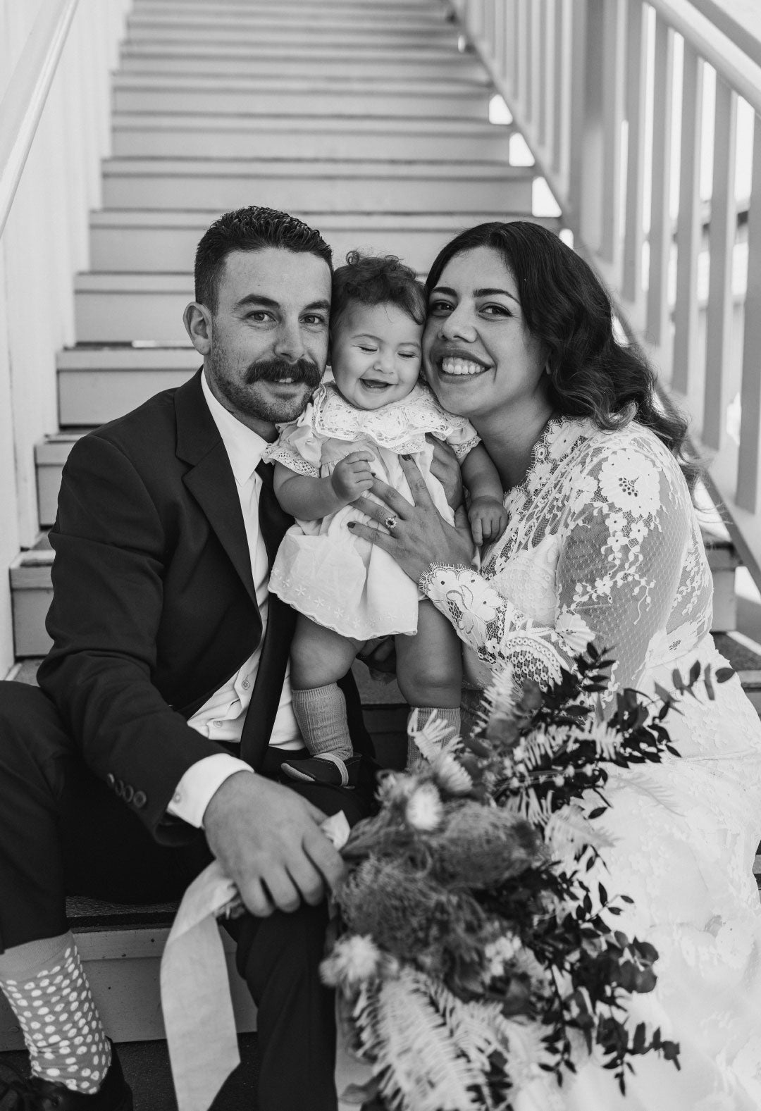Bride and Groom holding laughing baby seated on staircase