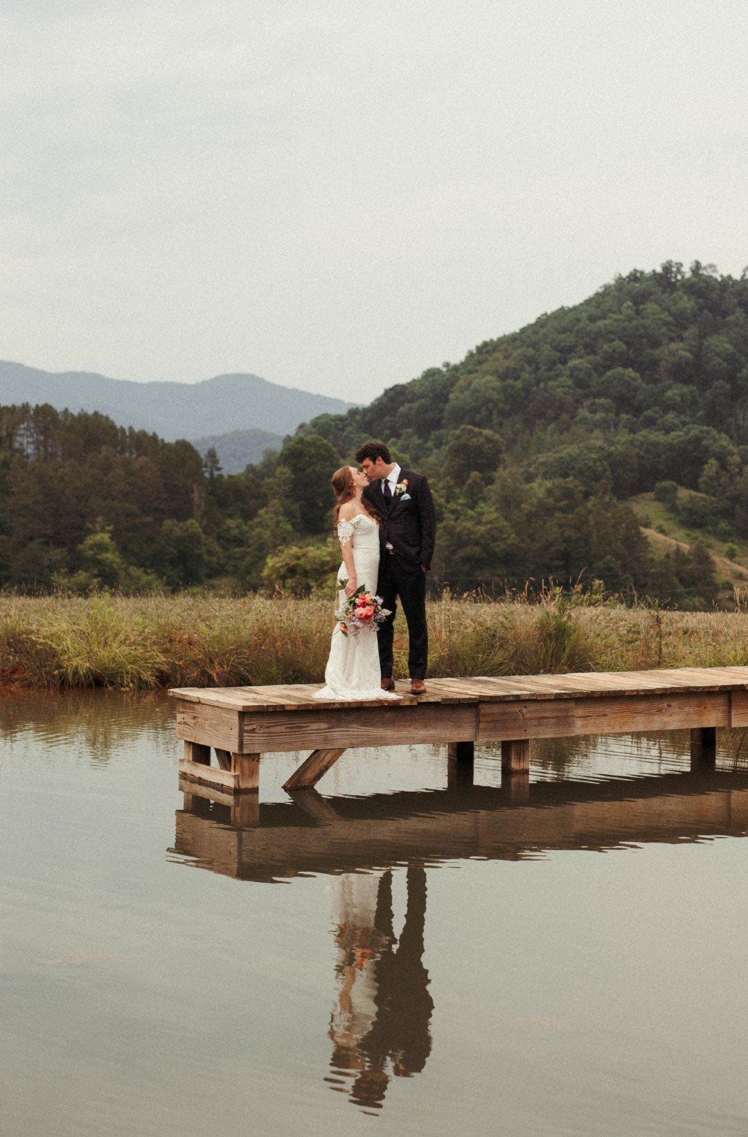 Bride and Groom Kissing standing on pond dock.