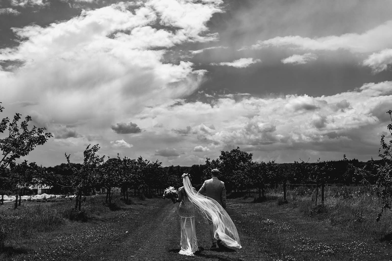 Black and white of bride and groom in open field with clouds in sky