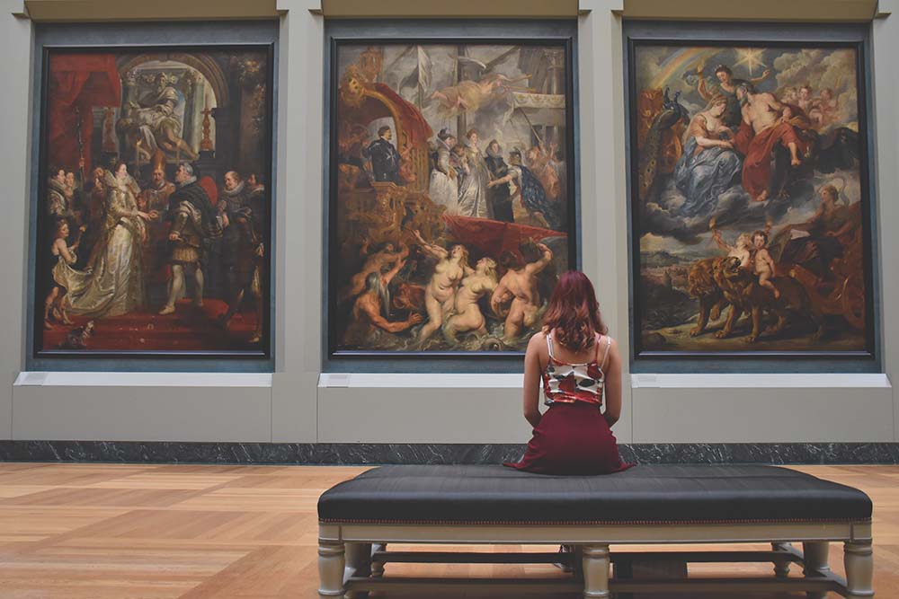 a girl sits in a museum looking at paintings